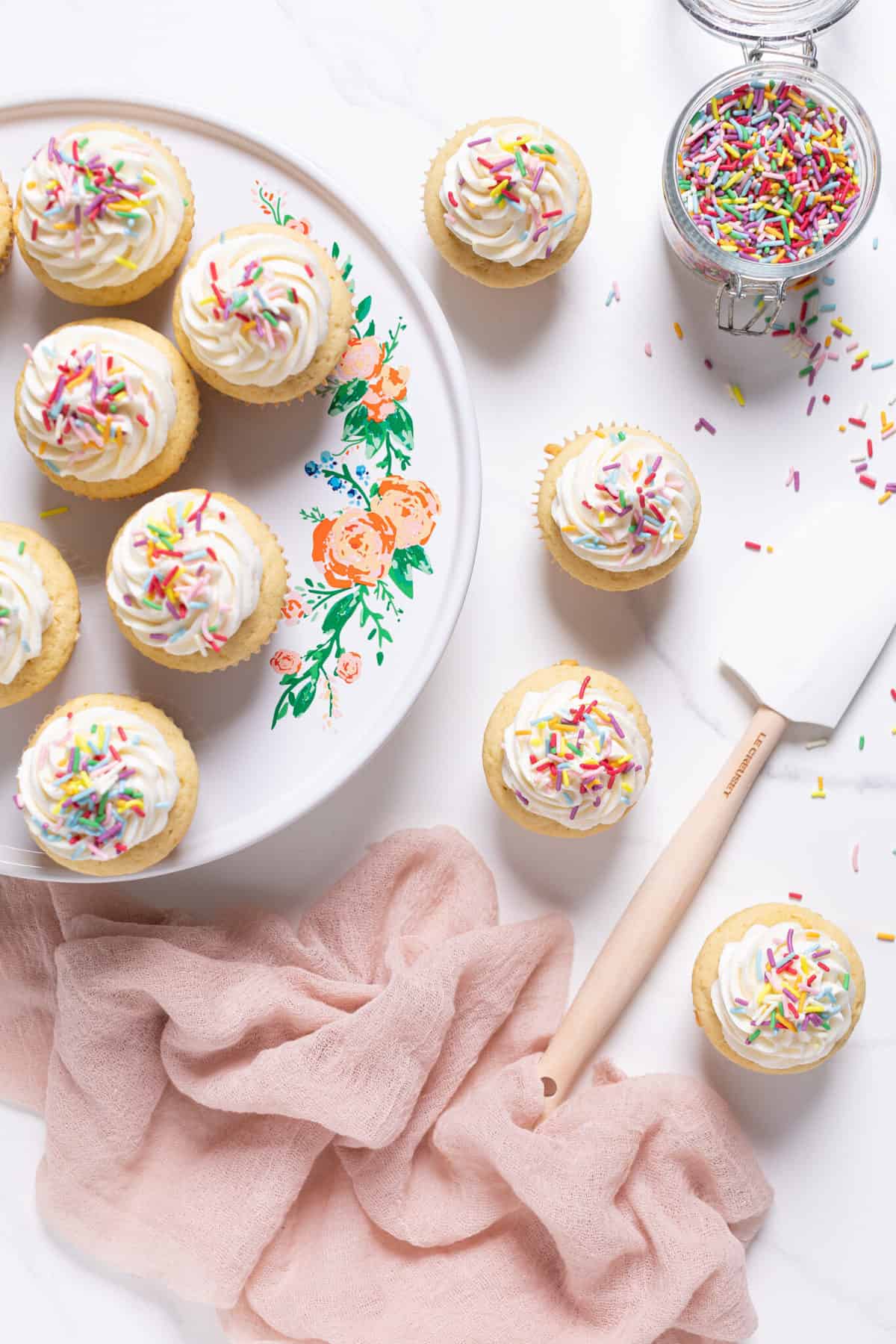 Vanilla Cupcakes with Buttercream Frosting on an elevated platter and a counter.