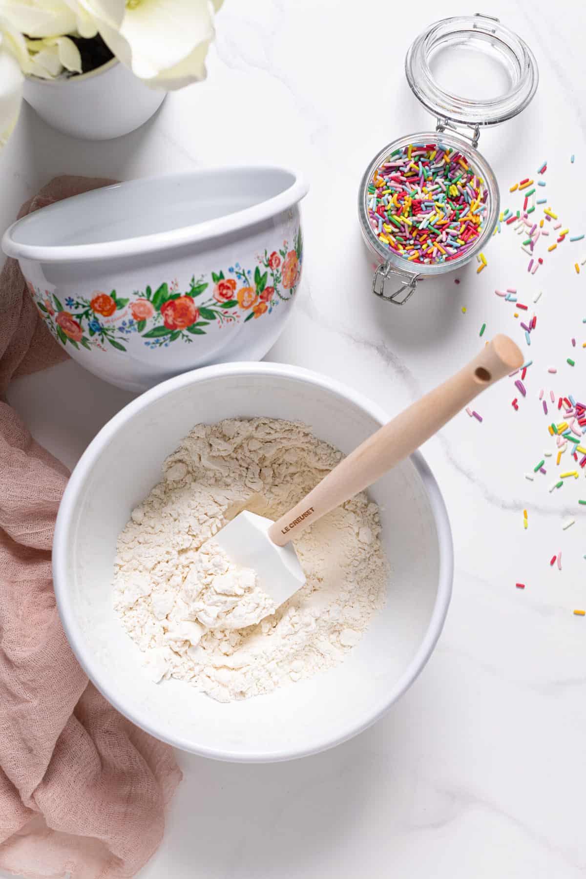 Bowl of dry cupcake ingredients next to a jar of colorful sprinkles.