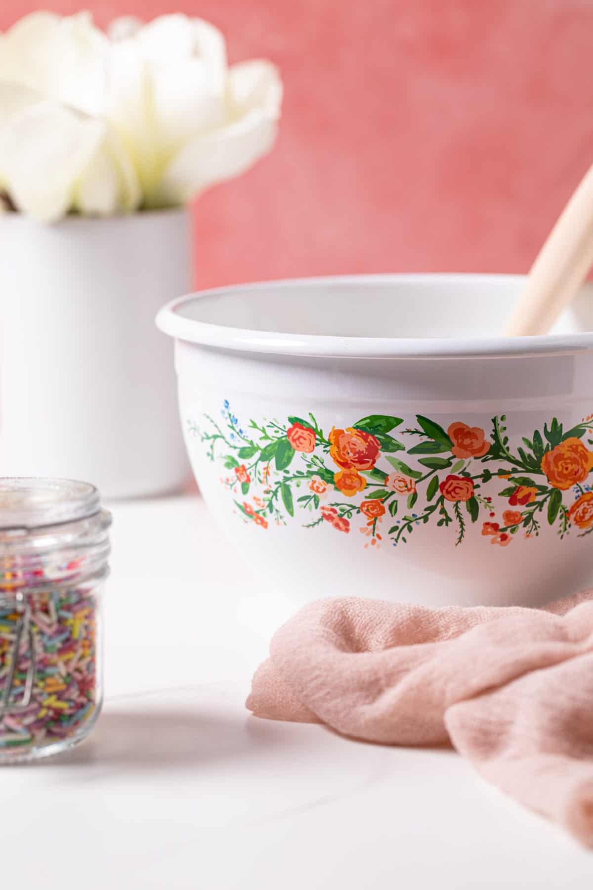 White, floral mixing bowl with a wooden spatula sticking out.