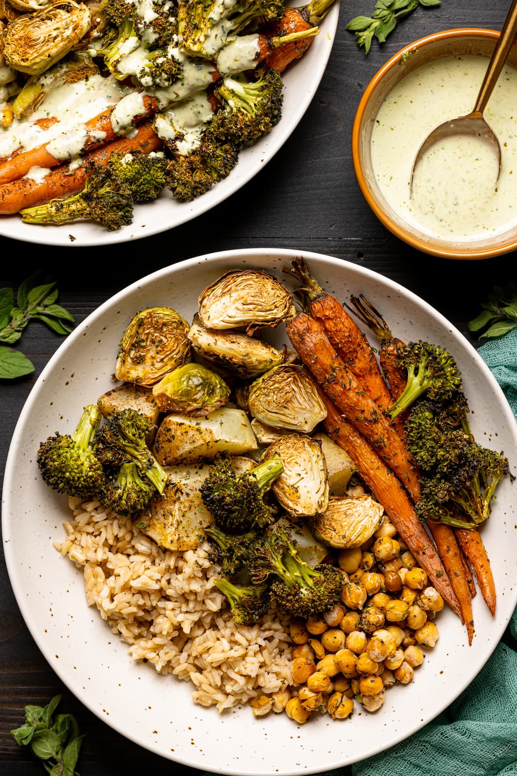 Veggies in two low bowls on a black table with pesto sauce and herbs.