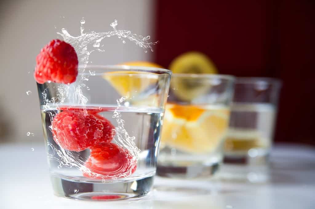 Raspberries splashing into a glass of water.