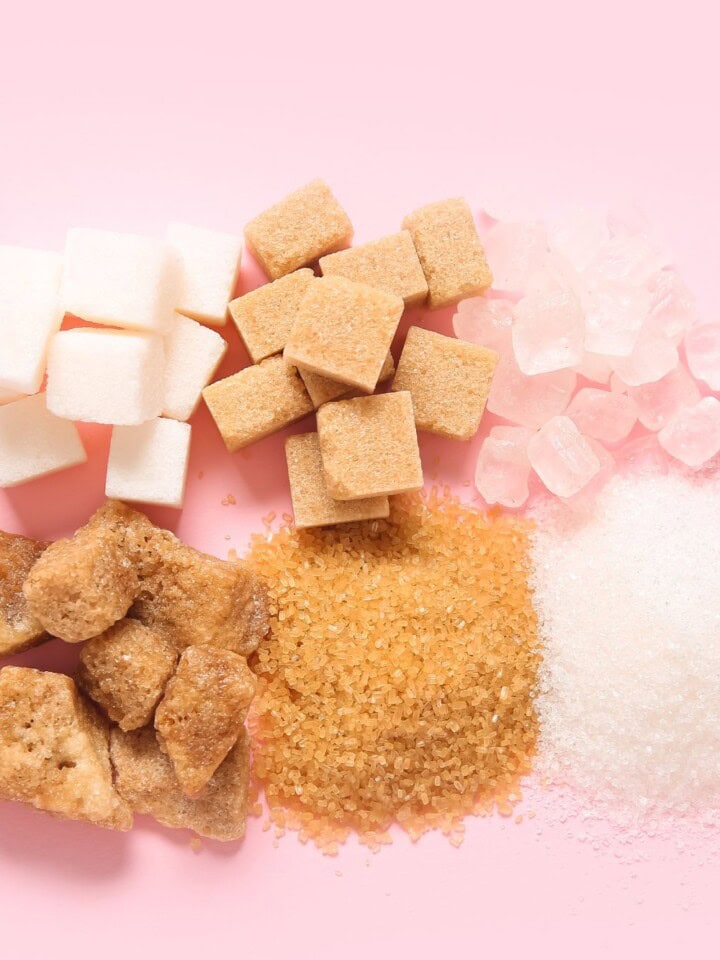 All different types of sugars on a pink background.