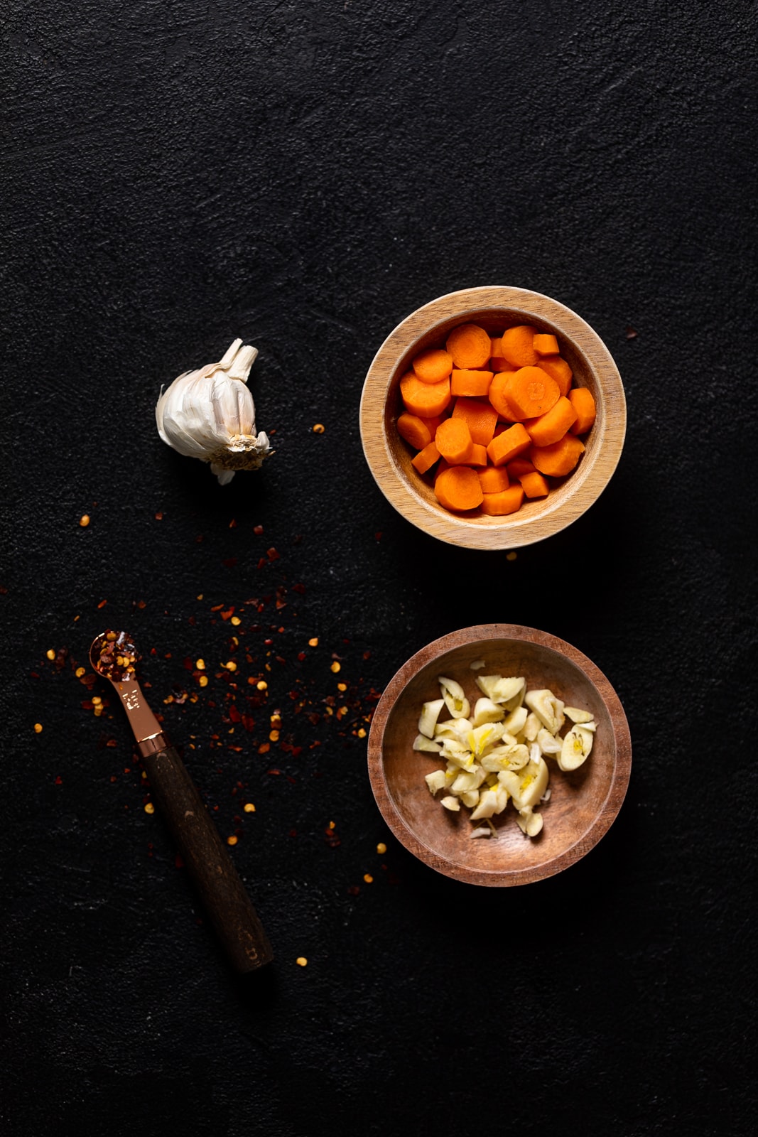 Bowls of carrots and garlic and spoon of crushed red pepper flakes