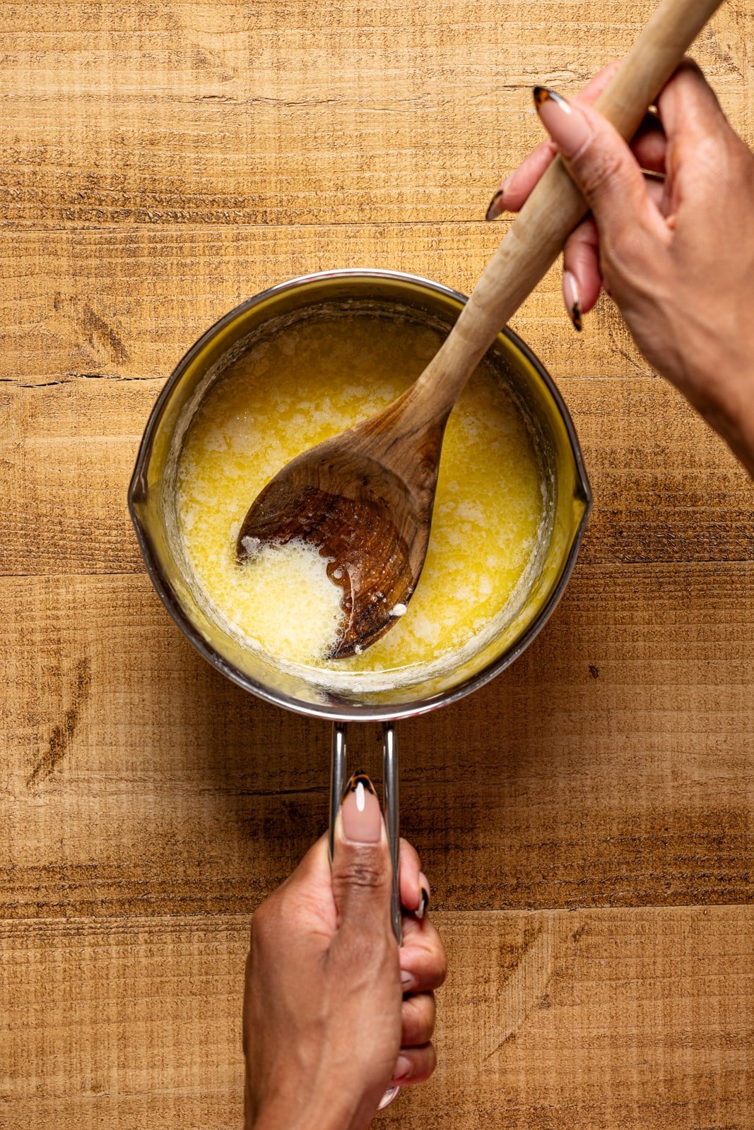 Butter milk mixture in a saucepan being held with a spoon.