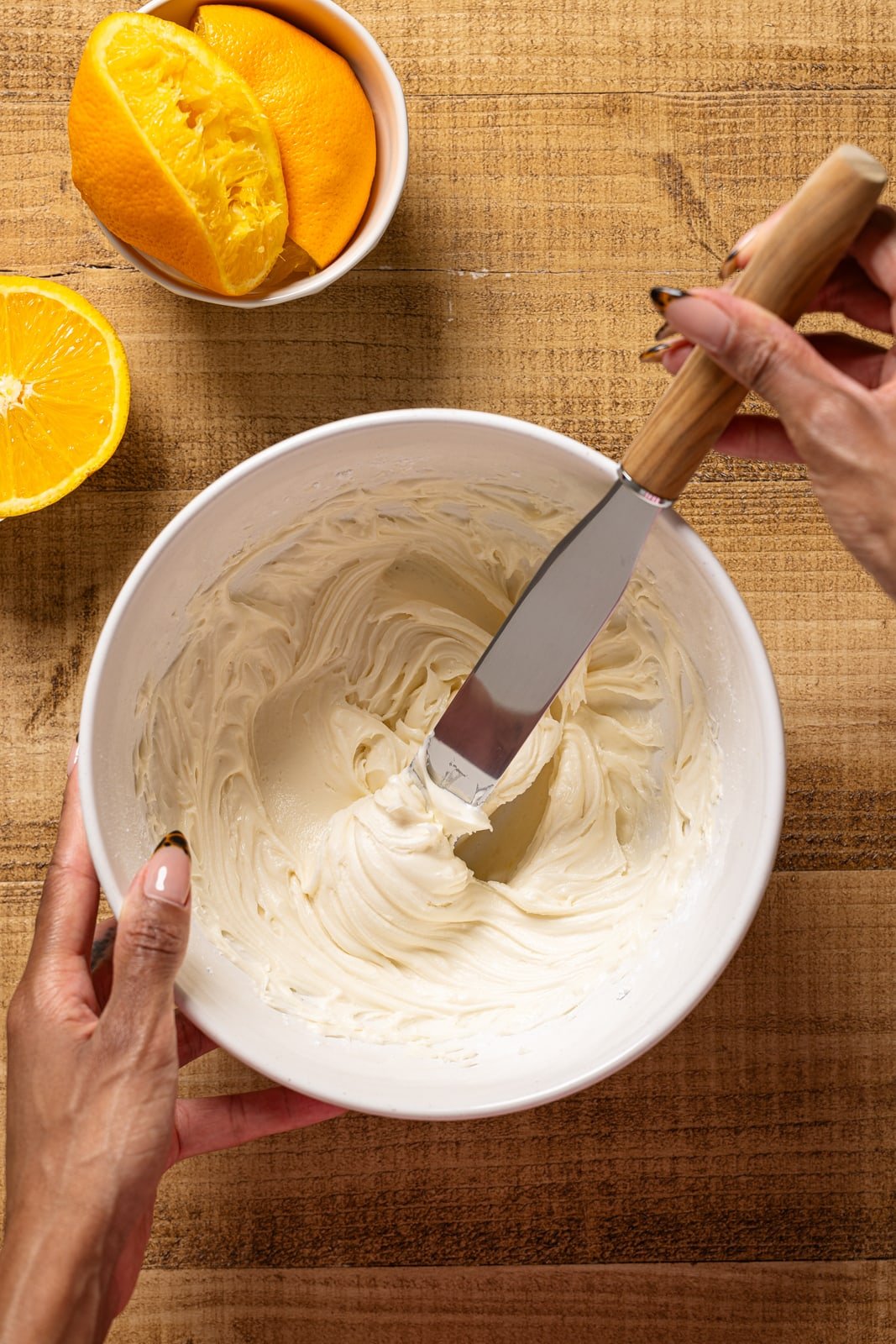 Orange frosting in a bowl being held with a spatula. 