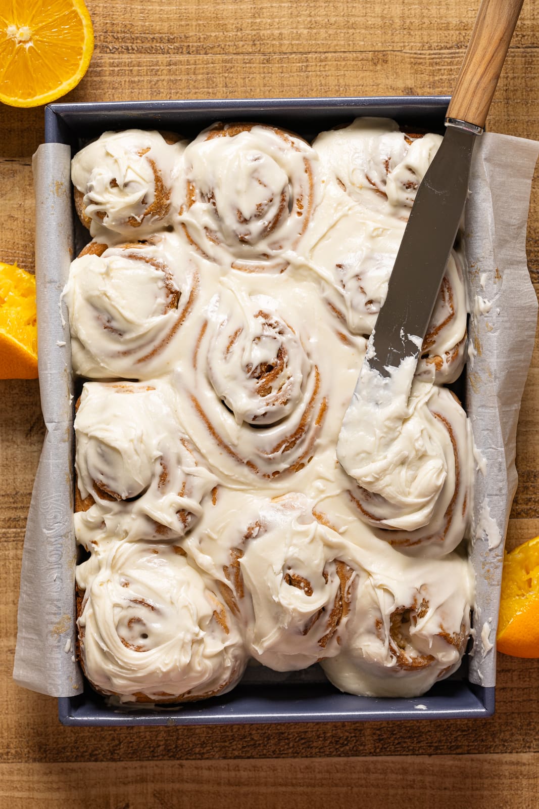Frosted cinnamon rolls in a baking dish with a spatula. 