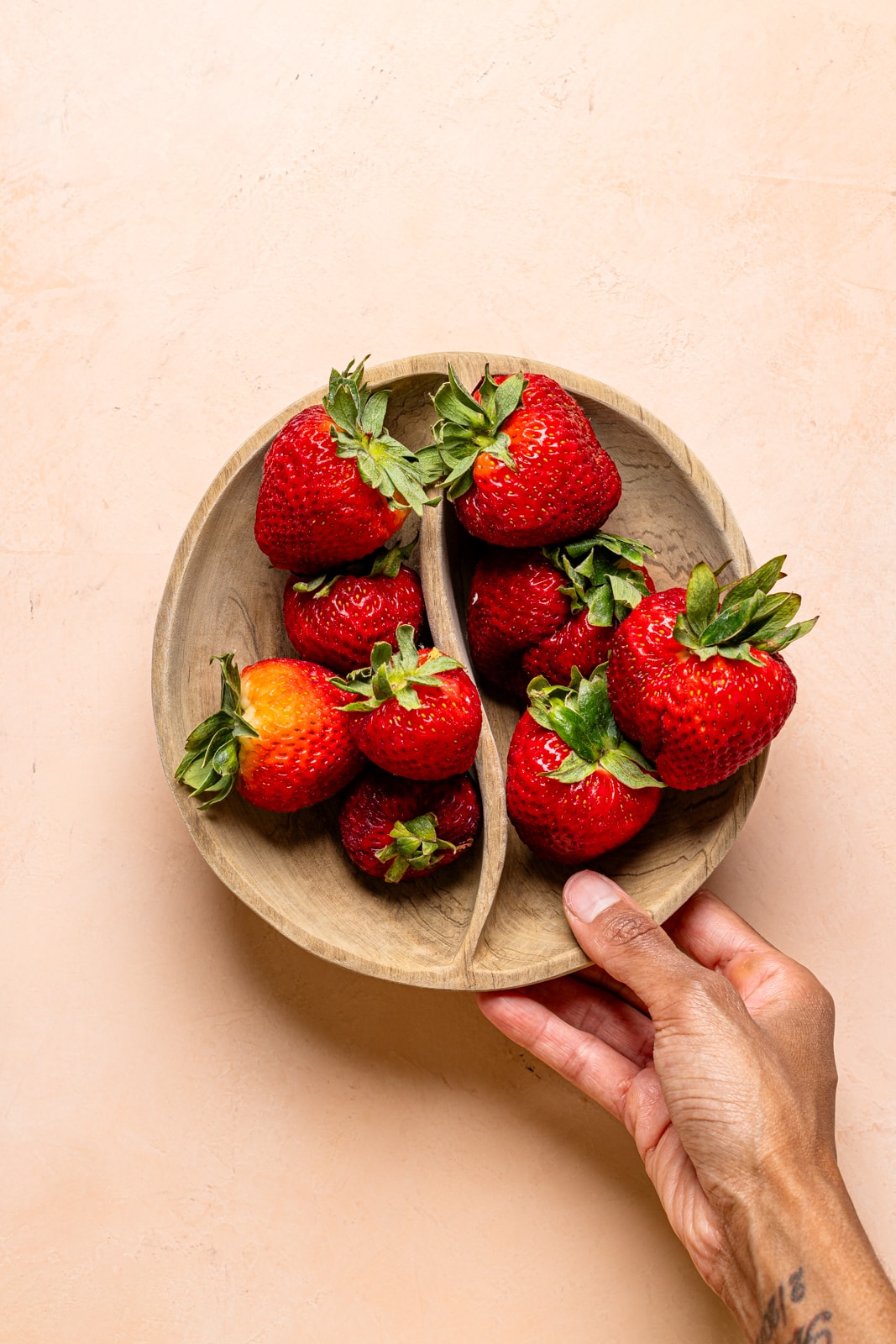 Fresh strawberries in a brown bowl on a peach table. 