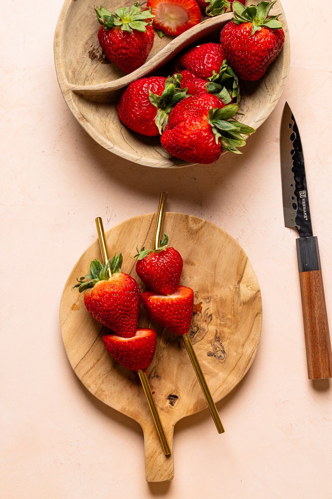 Fresh strawberries in a brown bowl and lined on straws with a knife. 