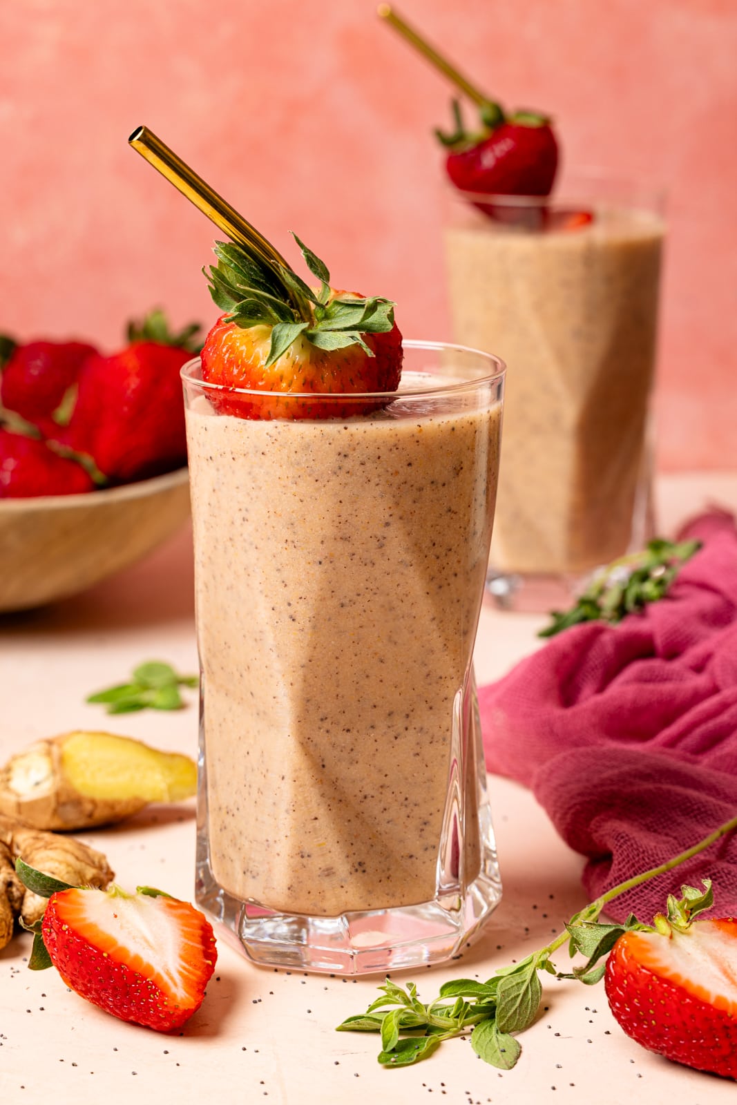 Two glasses with smoothies, fresh strawberries, and ginger on a peach table.