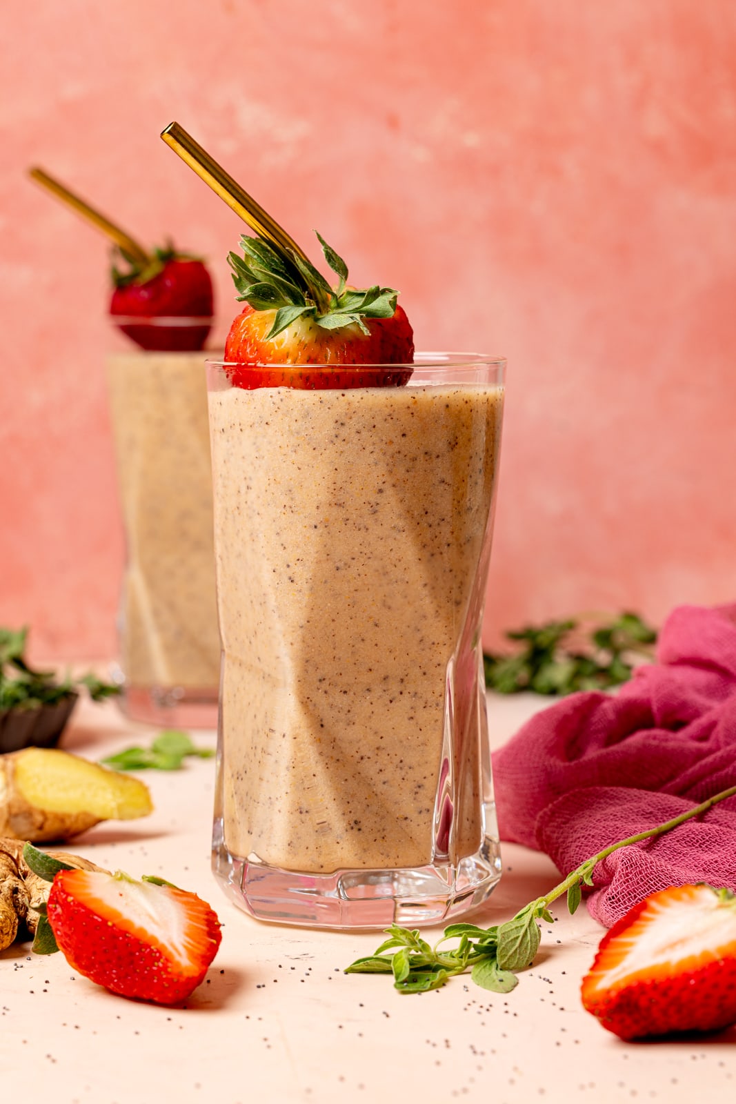 Two glasses of smoothies with sliced strawberries with a pink background. 