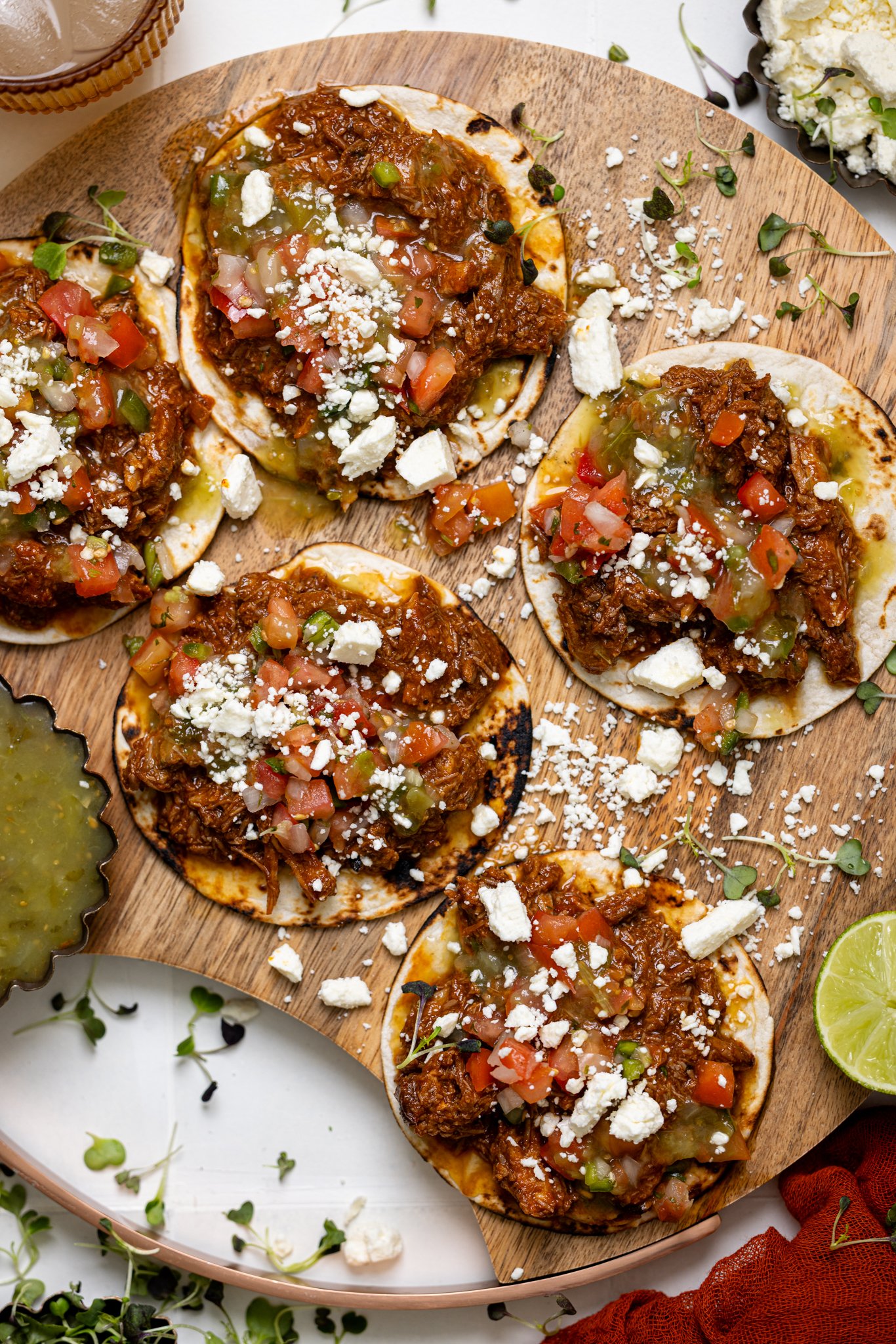 BBQ Braised Rib Street Tacos on a wooden board with sauces and garnish.