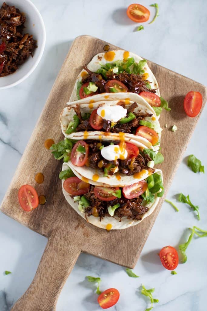 Wooden board topped with four Sweet Heat Barbeque Braised Rib Tacos.