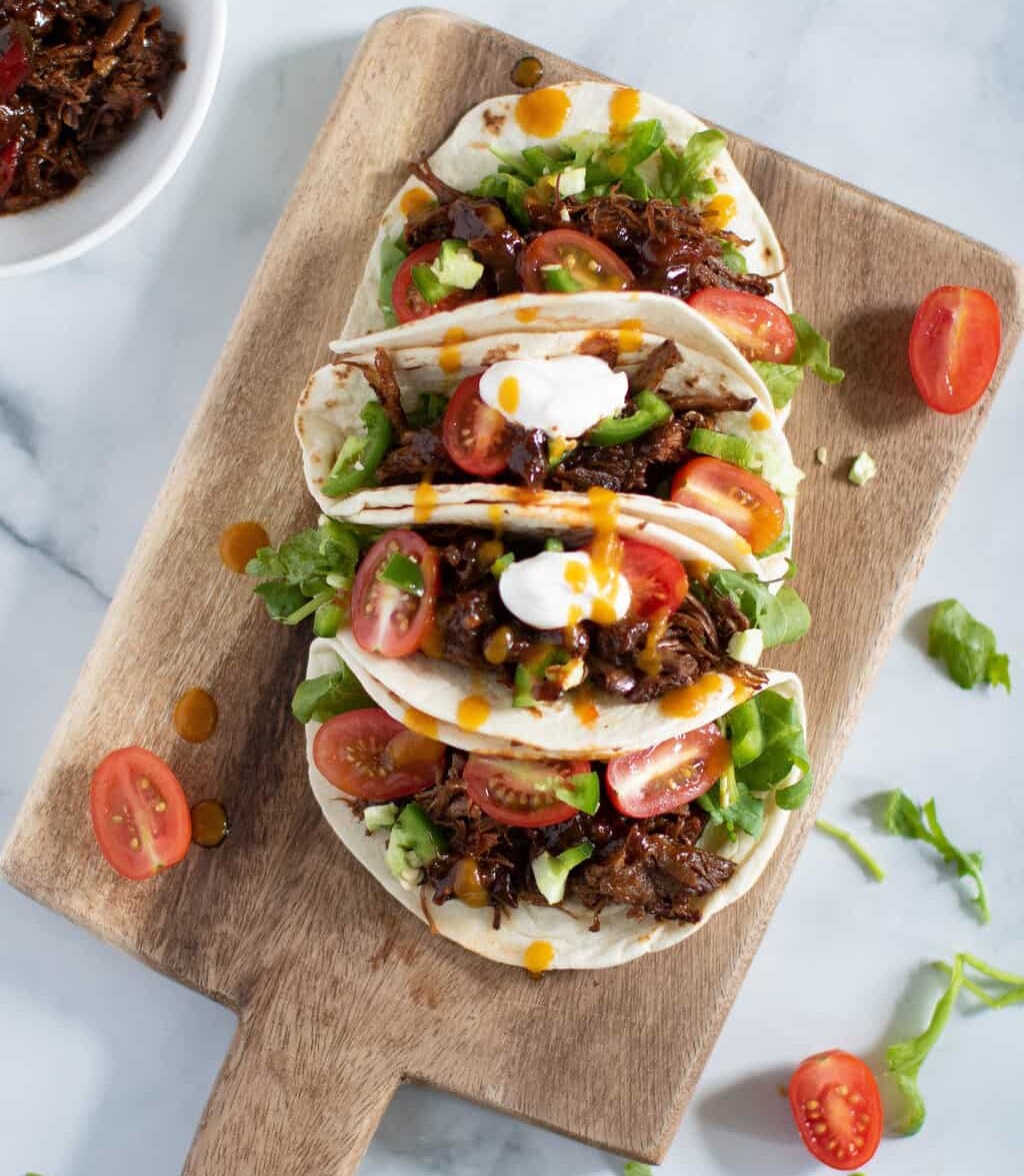 Wooden board topped with four Sweet Heat Barbeque Braised Rib Tacos.