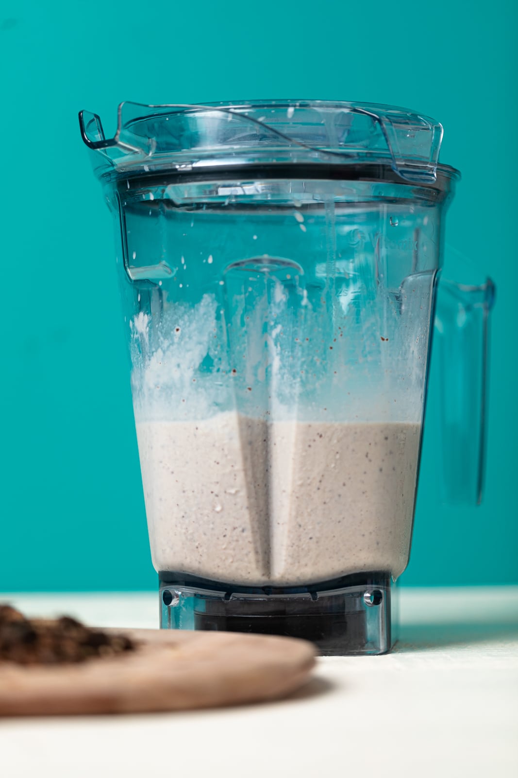 Blended milkshake in a blender on a white table with a bright blue background.