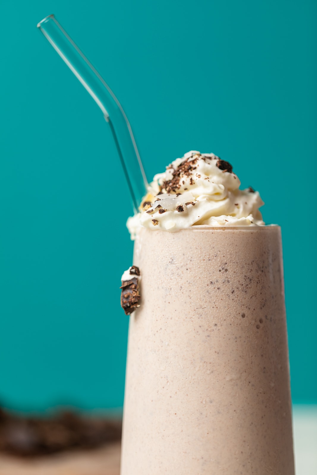 Up close shot of milkshake in a tall glass with whipped cream and cookie pieces on top.