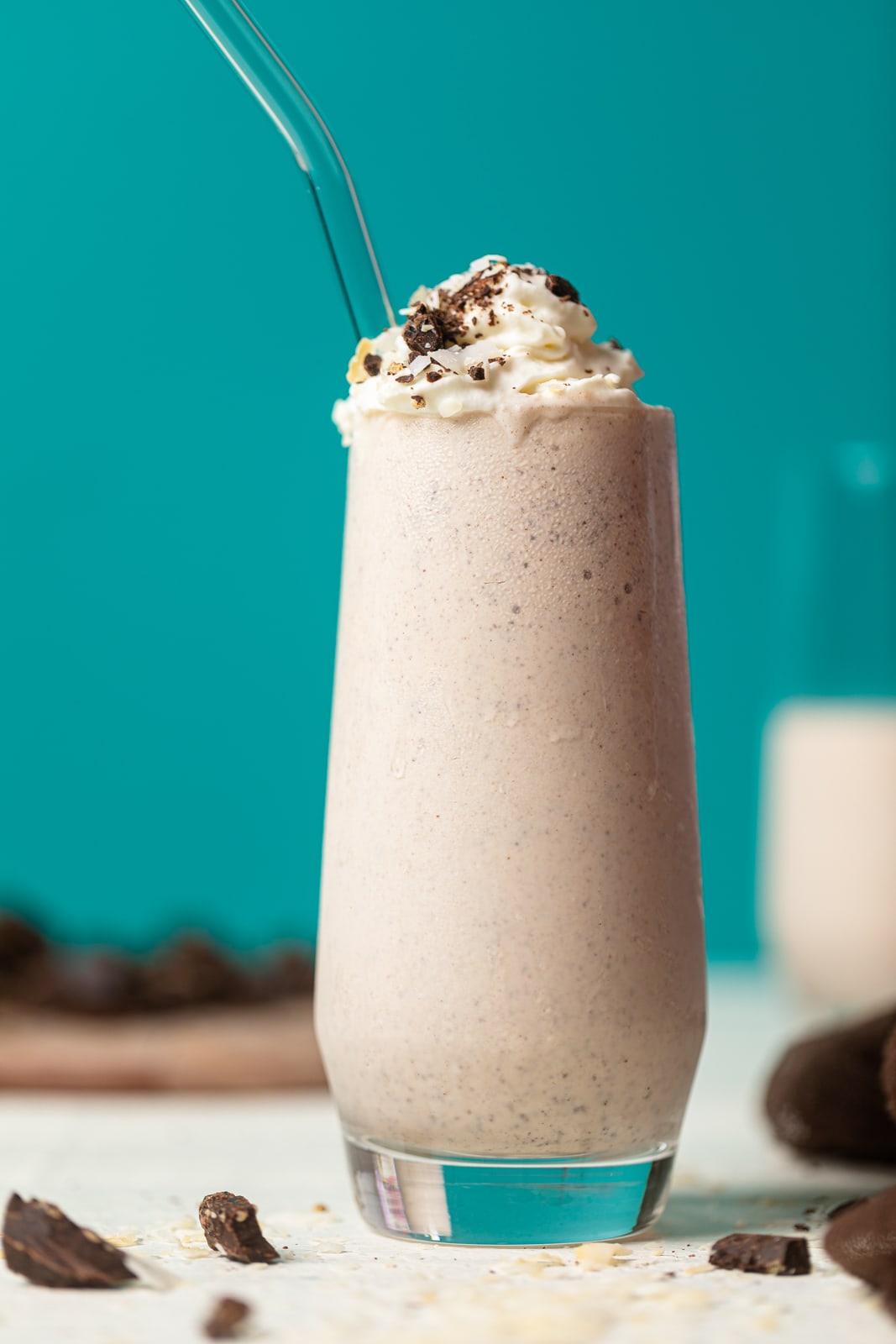 Milkshake in a tall glass with a glass straw topped with cookie pieces with a bright blue background.