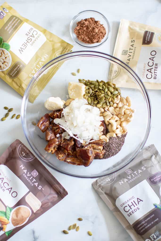 Bowl of ingredients surrounded by bags of Nativas cacao butter, cacao powder, cashews, and chia seeds.