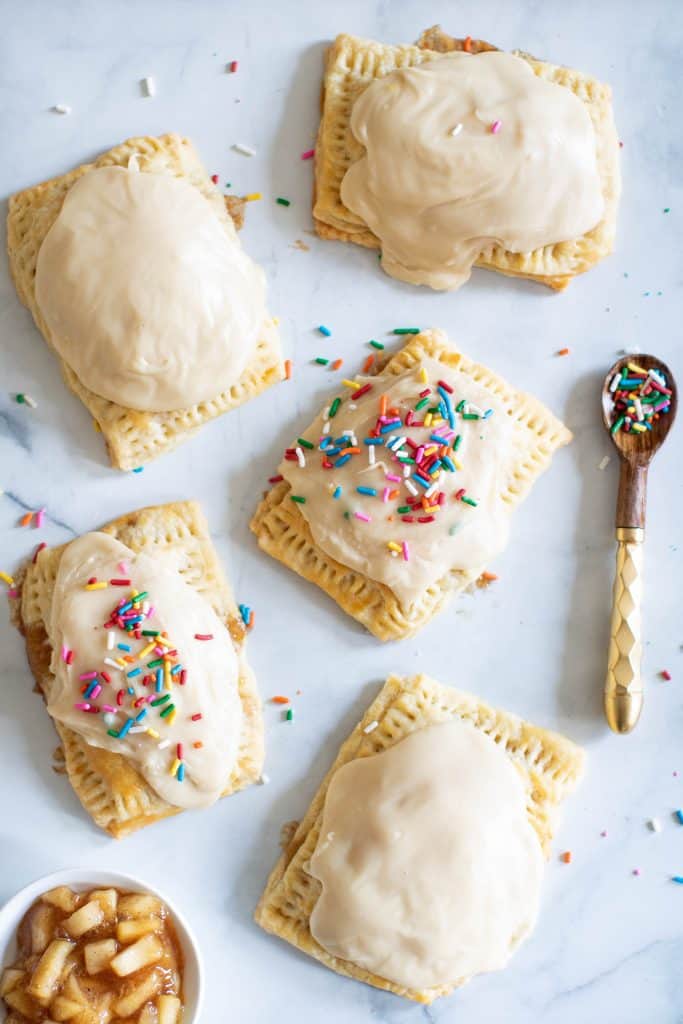 Vegan Apple-Cinnamon Pop Tarts on a table with a spoon of sprinkles.