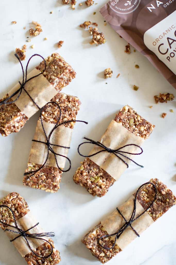 No-Bake Cacao Date Loaded Energy Bars wrapped with paper and tied with twine on a marble countertop.