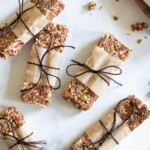 No-Bake Cacao Date Loaded Energy Bars wrapped with paper and tied with twine on a marble countertop.