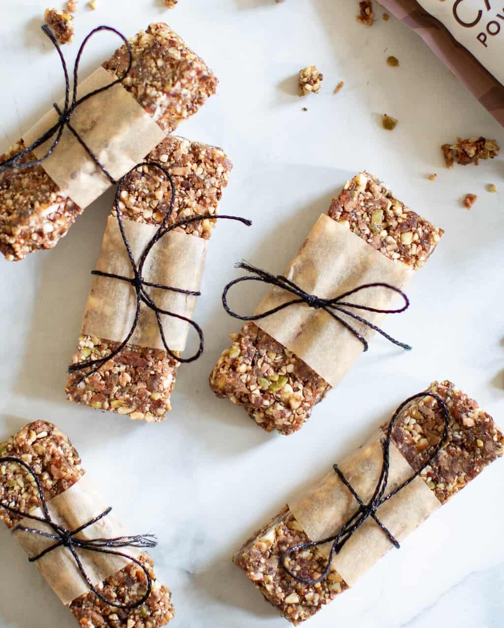 No-Bake Cacao Date Loaded Energy Bars wrapped with paper and tied with twine on a marble countertop.
