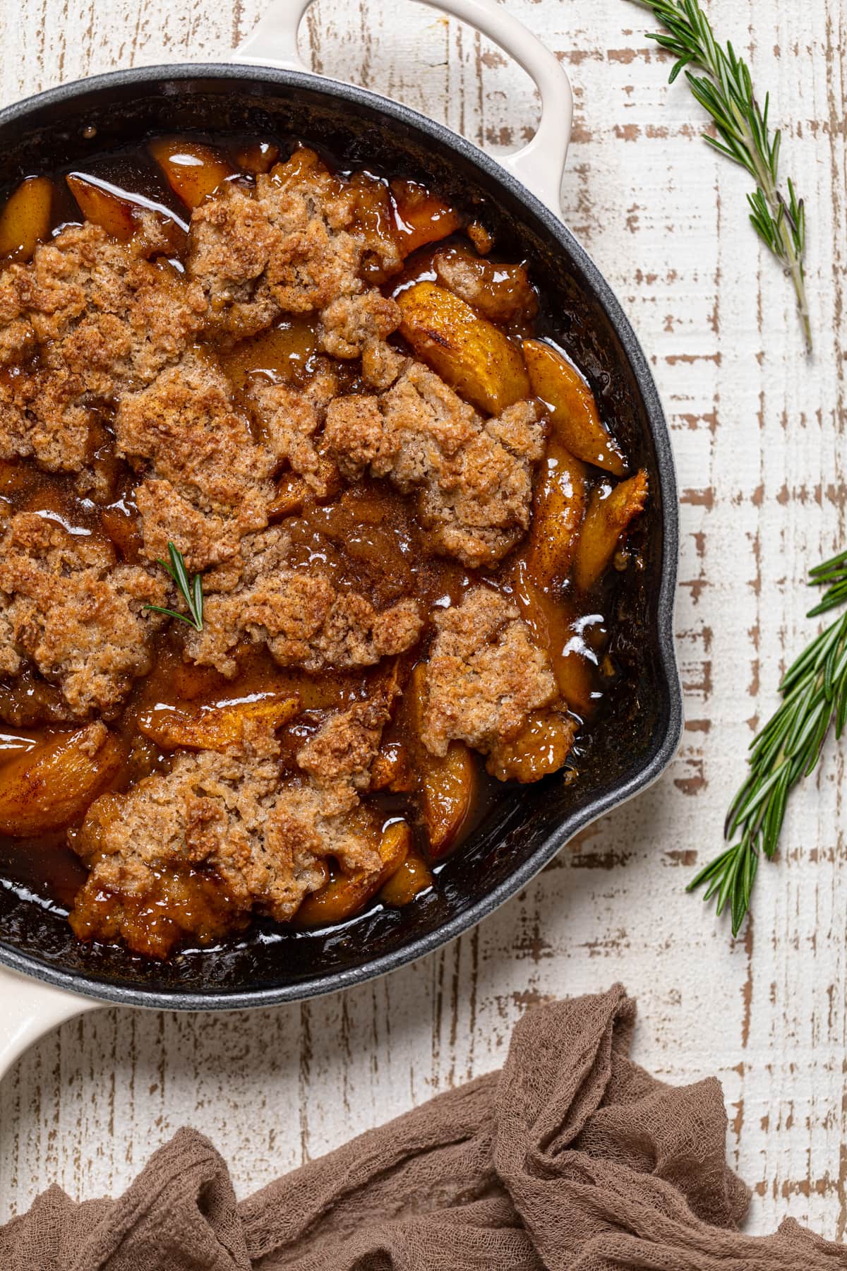 Vegan Southern Peach Cobbler on a table with sprigs of rosemary.