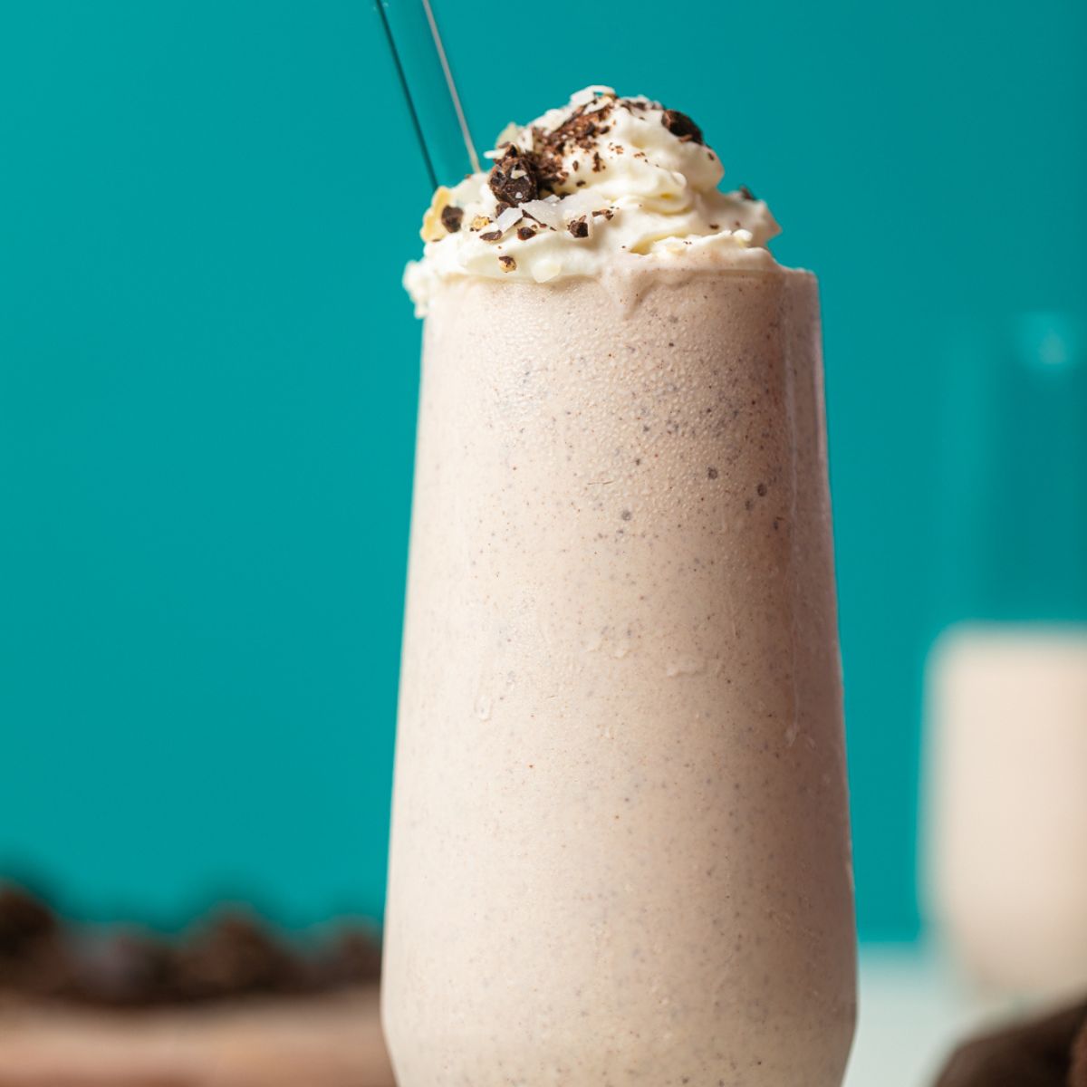 Milkshake in a tall glass with a glass straw topped with cookie pieces with a bright blue background.