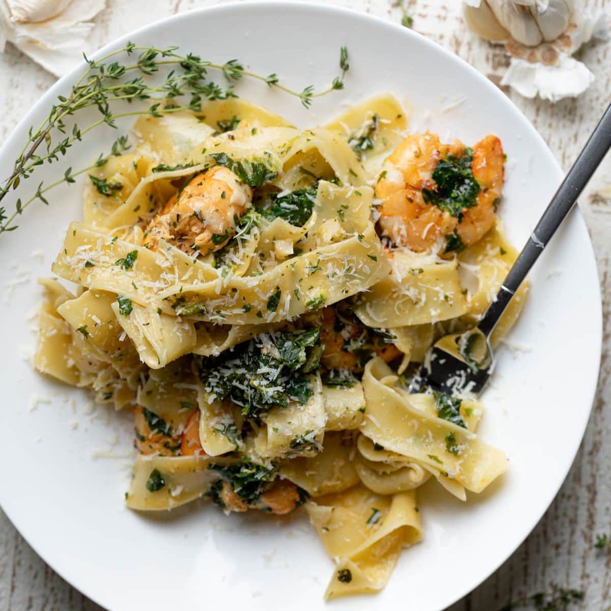 Shrimp pasta on a white plate with herbs and a fork.