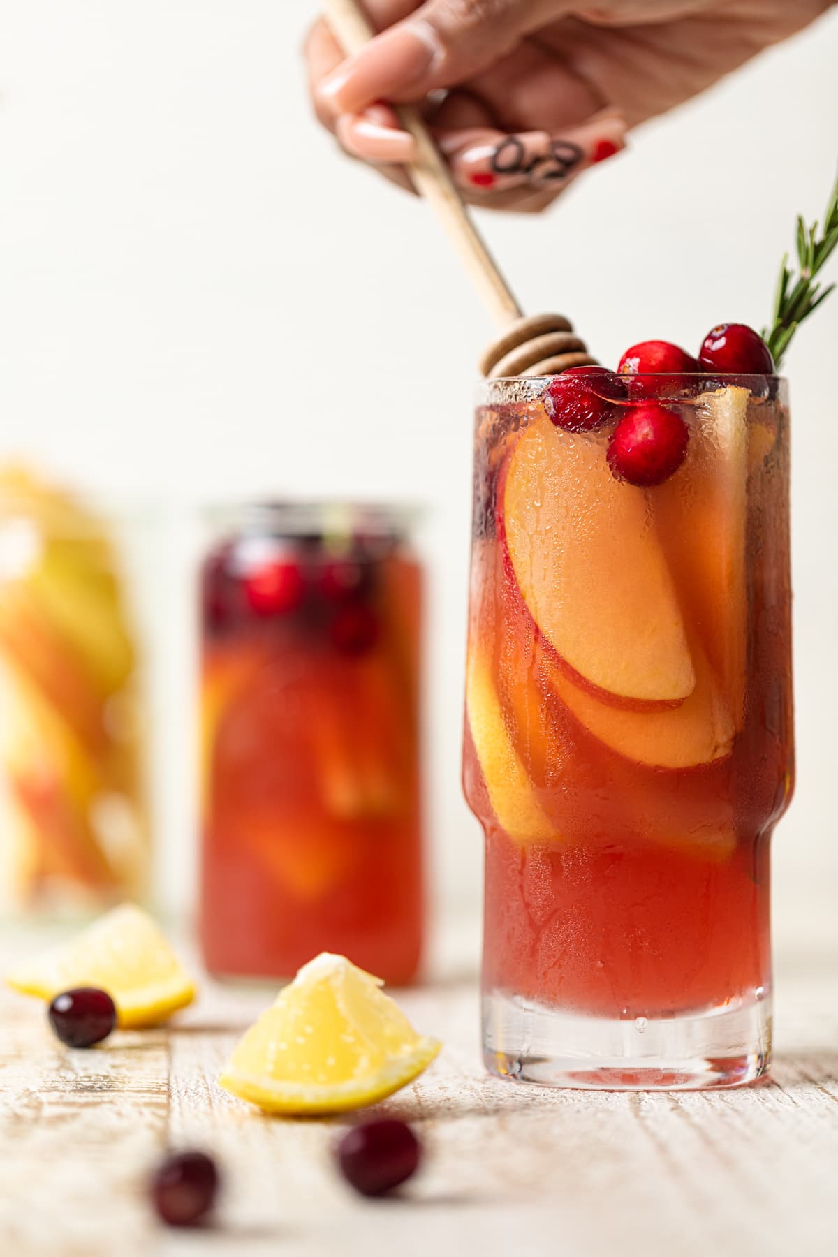 Glasses of Apple Cranberry Ginger Lemon Detox Juice on a table with lemon pieces and cranberries.