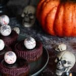 Plate of Halloween Graveyard Cheesecake Bites next to a pumpkin and skulls.