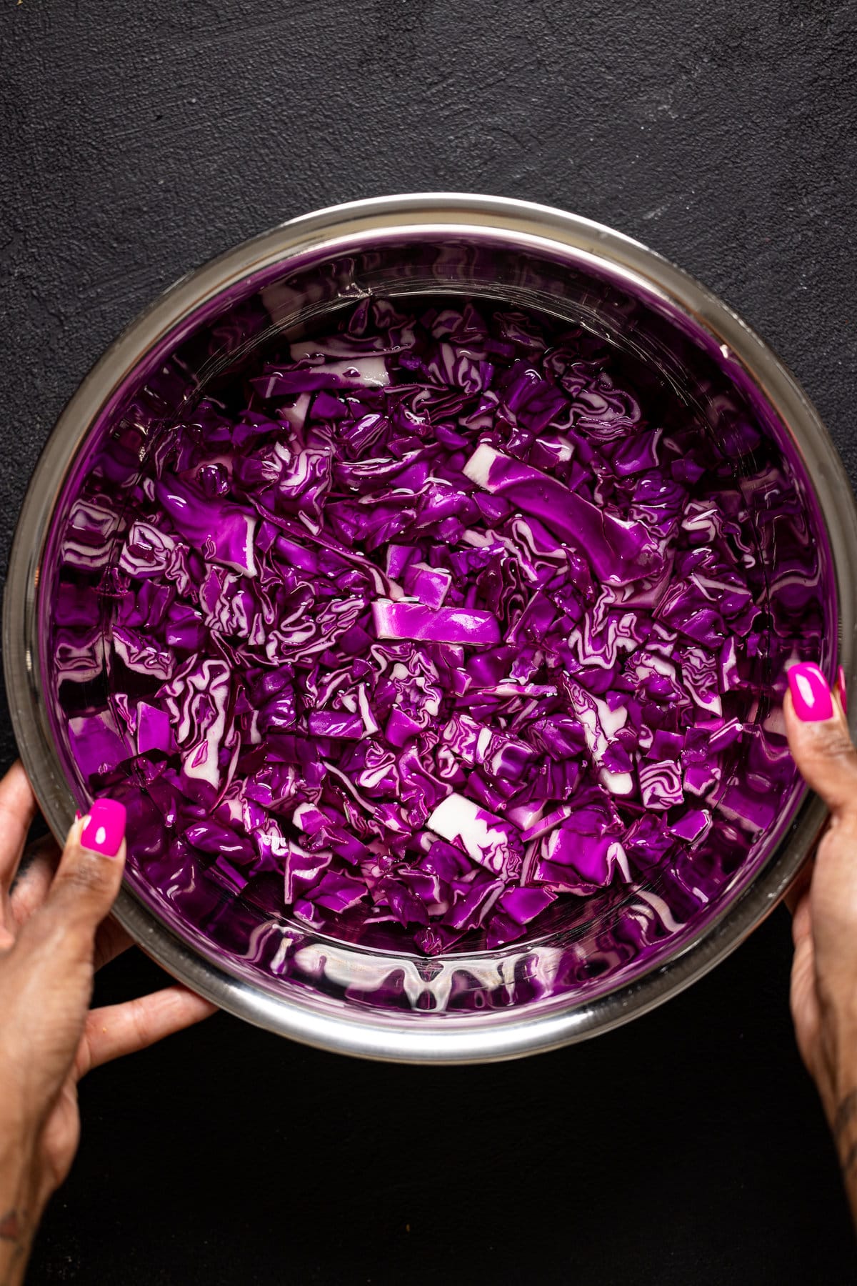 Bowl of shredded purple cabbage and water being held by two hands