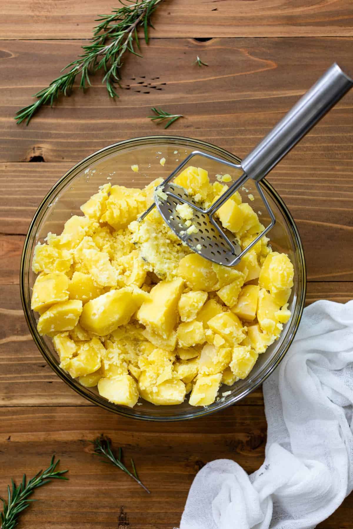 Potato masher in a glass bowl of potatoes.