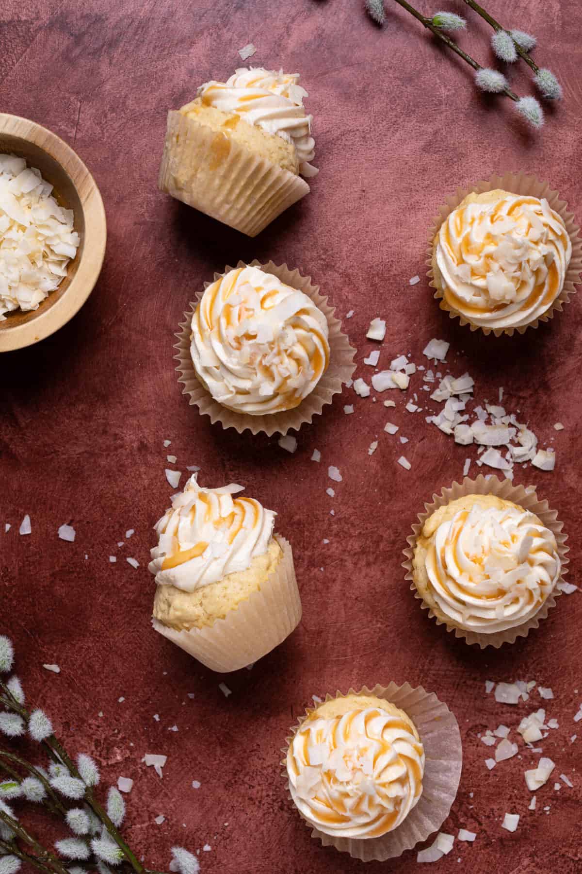 Easy Caramel Coconut Cupcakes in paper wrappers on a red surface.