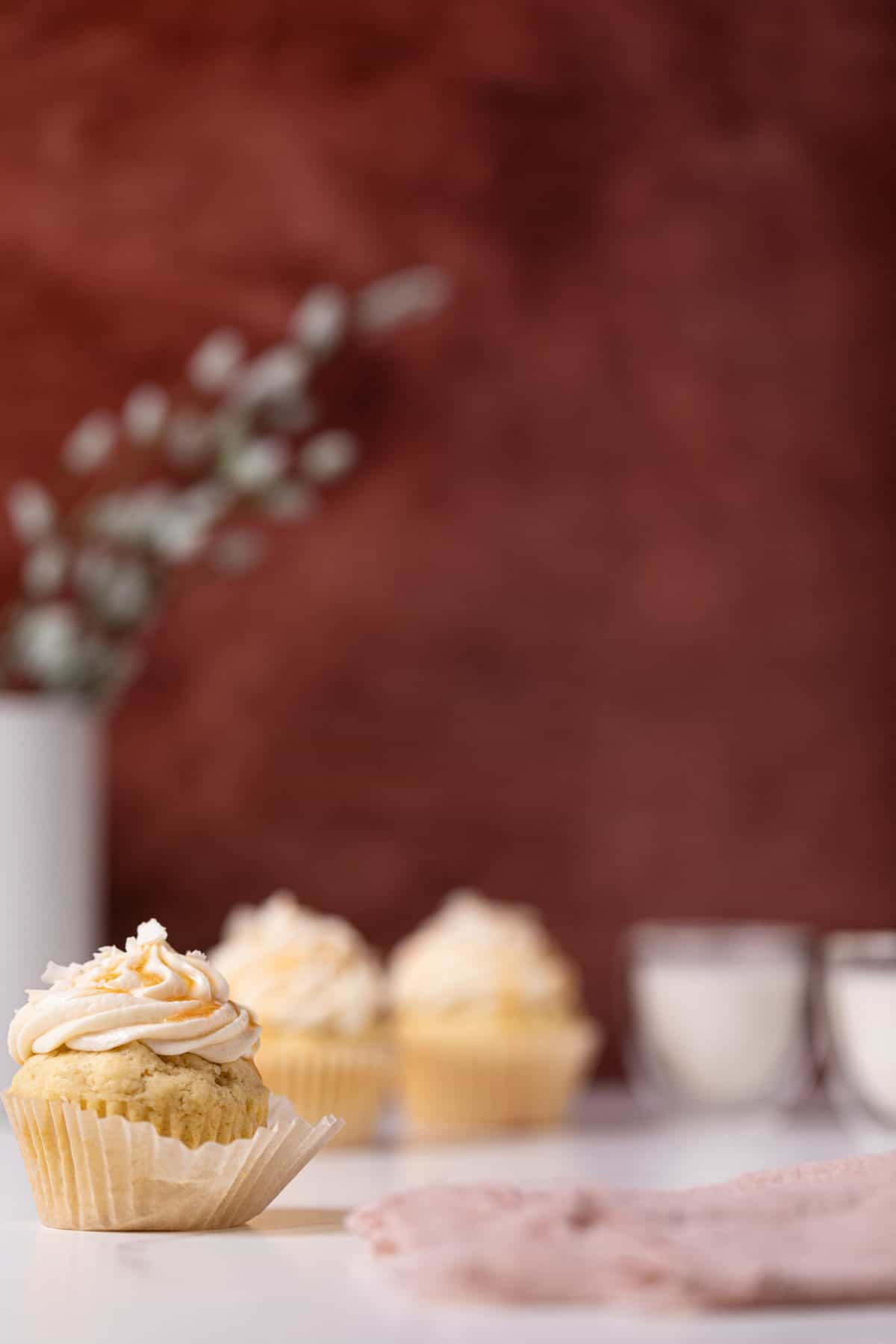 Easy Caramel Coconut Cupcakes in paper wrappers on a white surface with a red background.