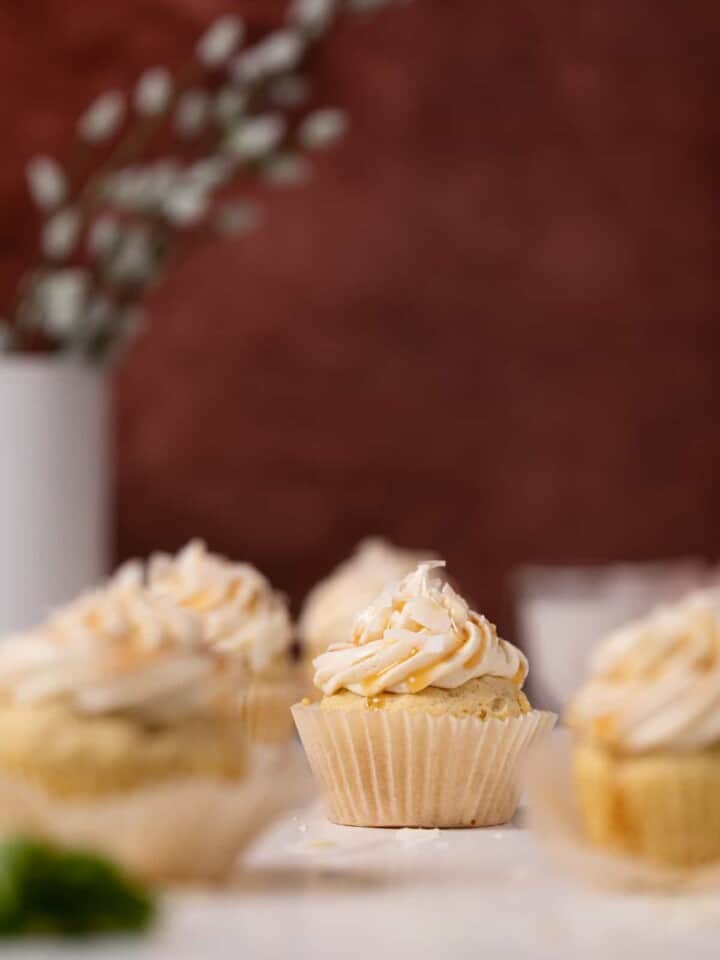Easy Caramel Coconut Cupcakes in paper wrappers on a white surface.