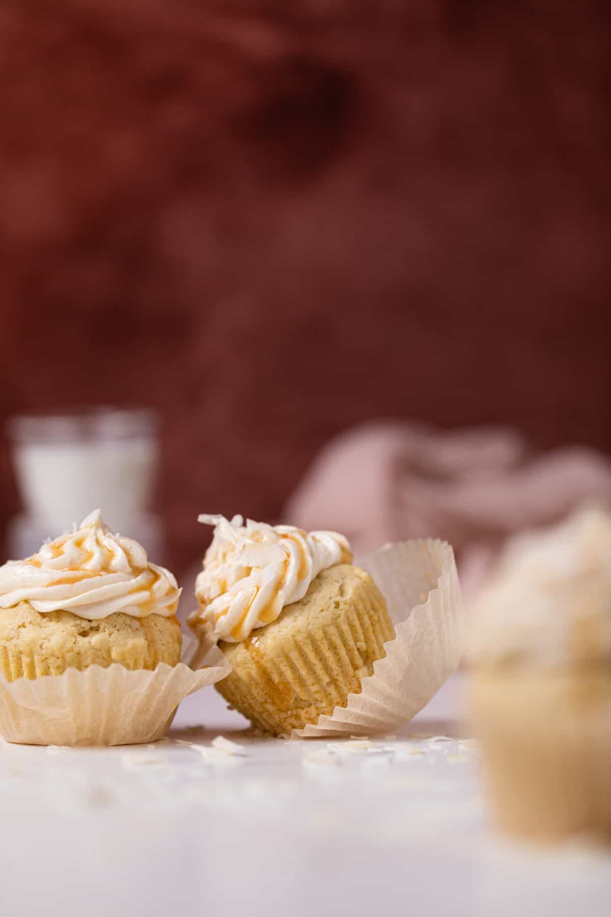 Easy Caramel Coconut Cupcakes in paper wrappers on a white surface.