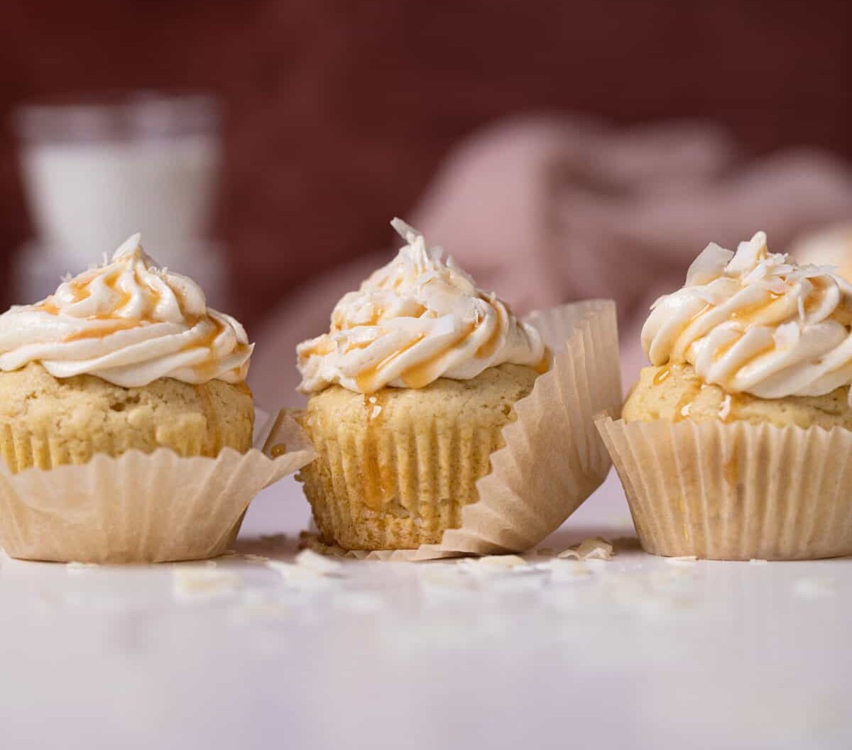 Easy Caramel Coconut Cupcakes in paper wrappers on a white surface.