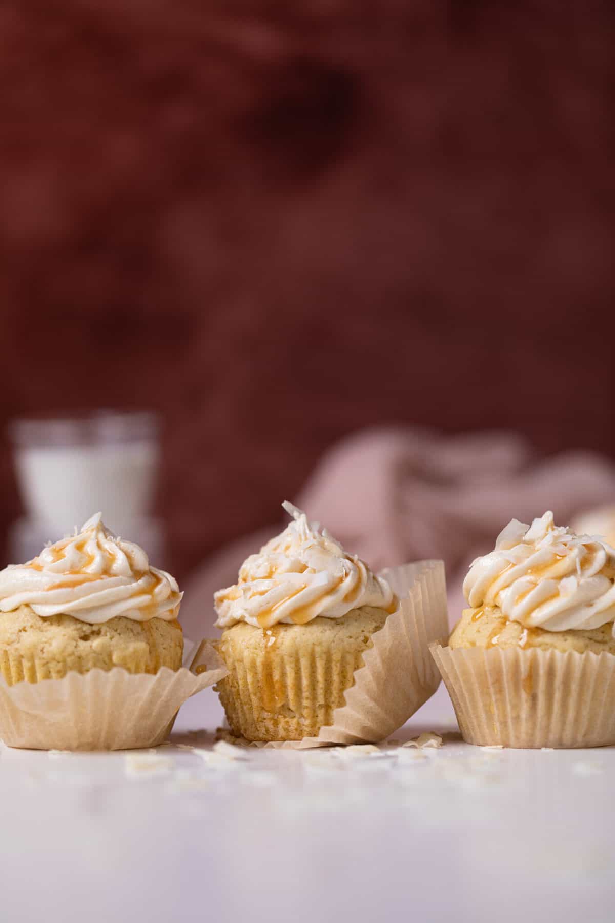 Easy Caramel Coconut Cupcakes in paper wrappers on a white surface.