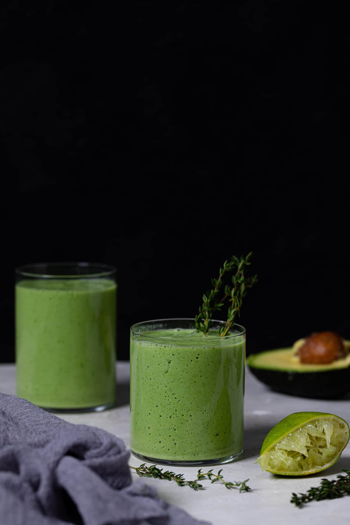 Super Green Detox Smoothies on a table with limes and an avocado.