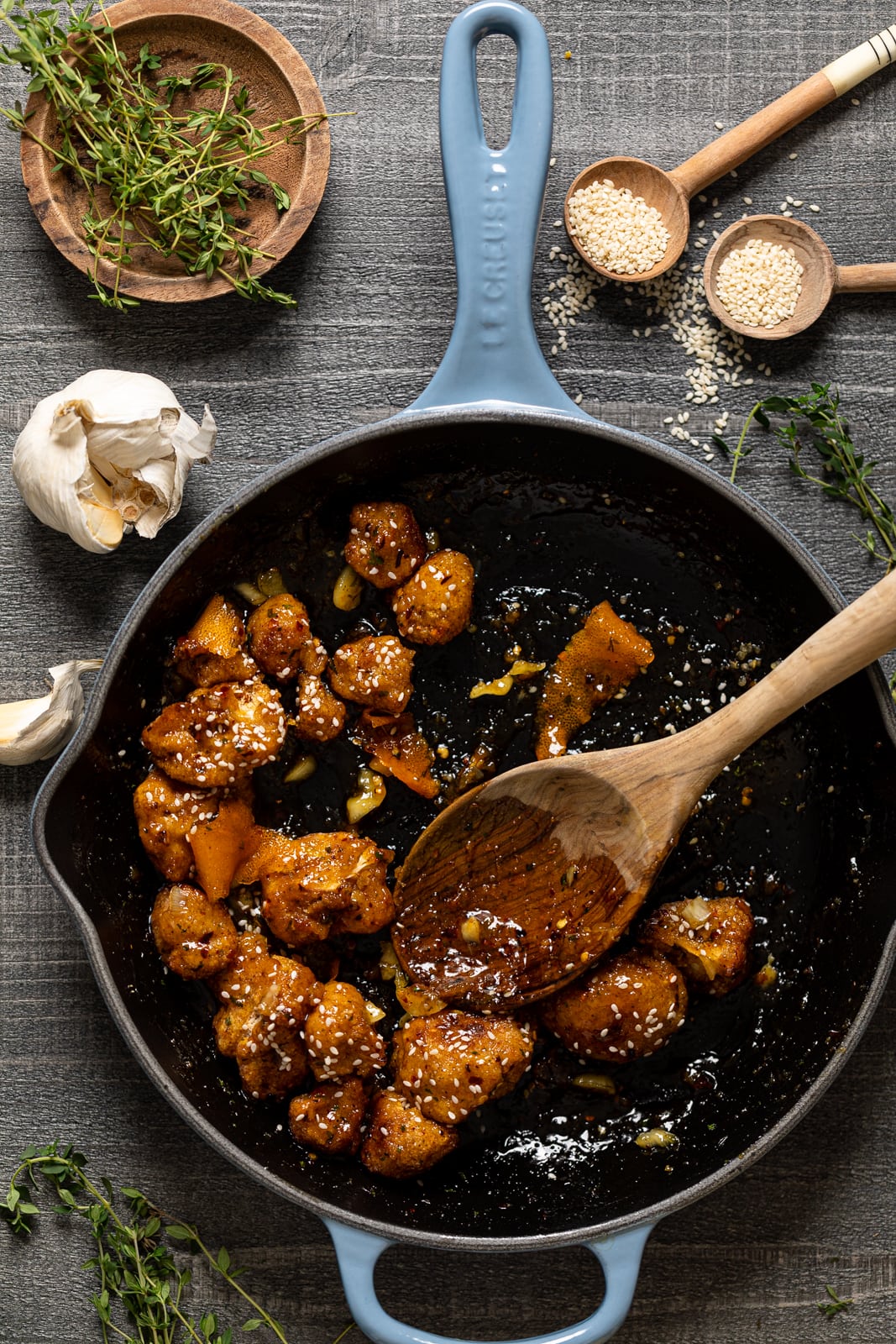 Wooden spoon stirring a skillet of Baked Sticky Orange Cauliflower