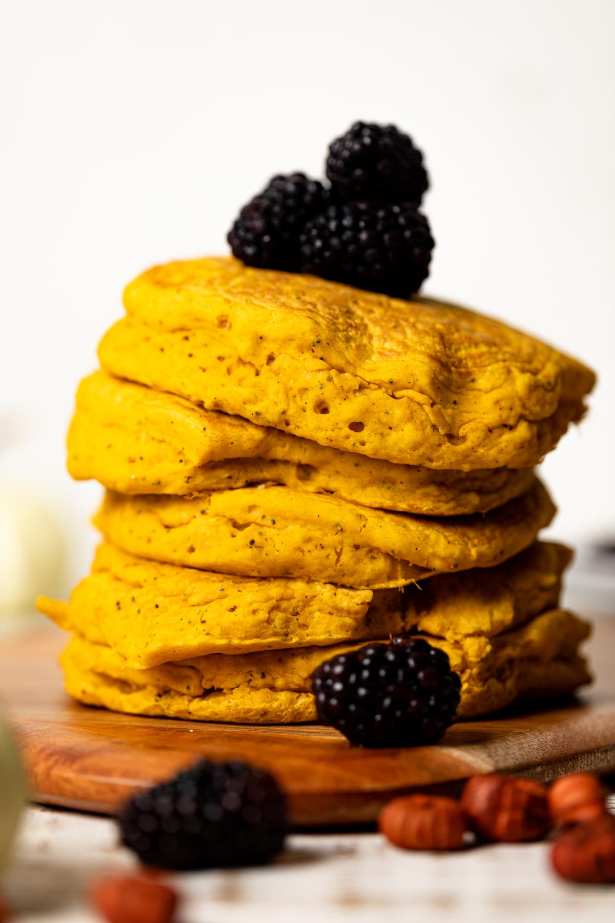 Stack of Vegan Pumpkin Poppyseed Pancakes topped with blackberries and on a wooden board