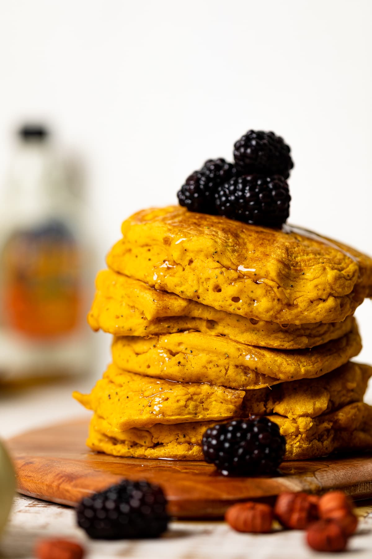 Stack of Vegan Pumpkin Poppyseed Pancakes topped with blackberries and syrup and on a wooden board