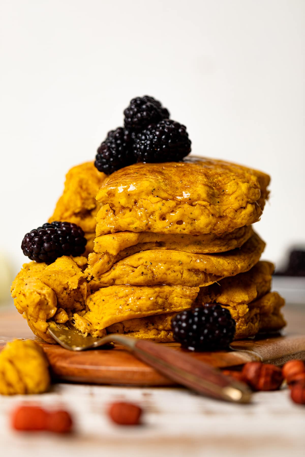 Stack of Vegan Pumpkin Poppyseed Pancakes topped with blackberries and on a wooden board with a fork