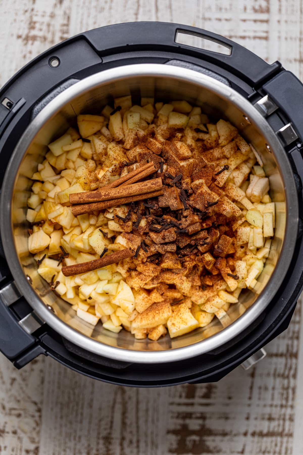 Slower cooker full of apple pieces, cinnamon sticks, and spices.