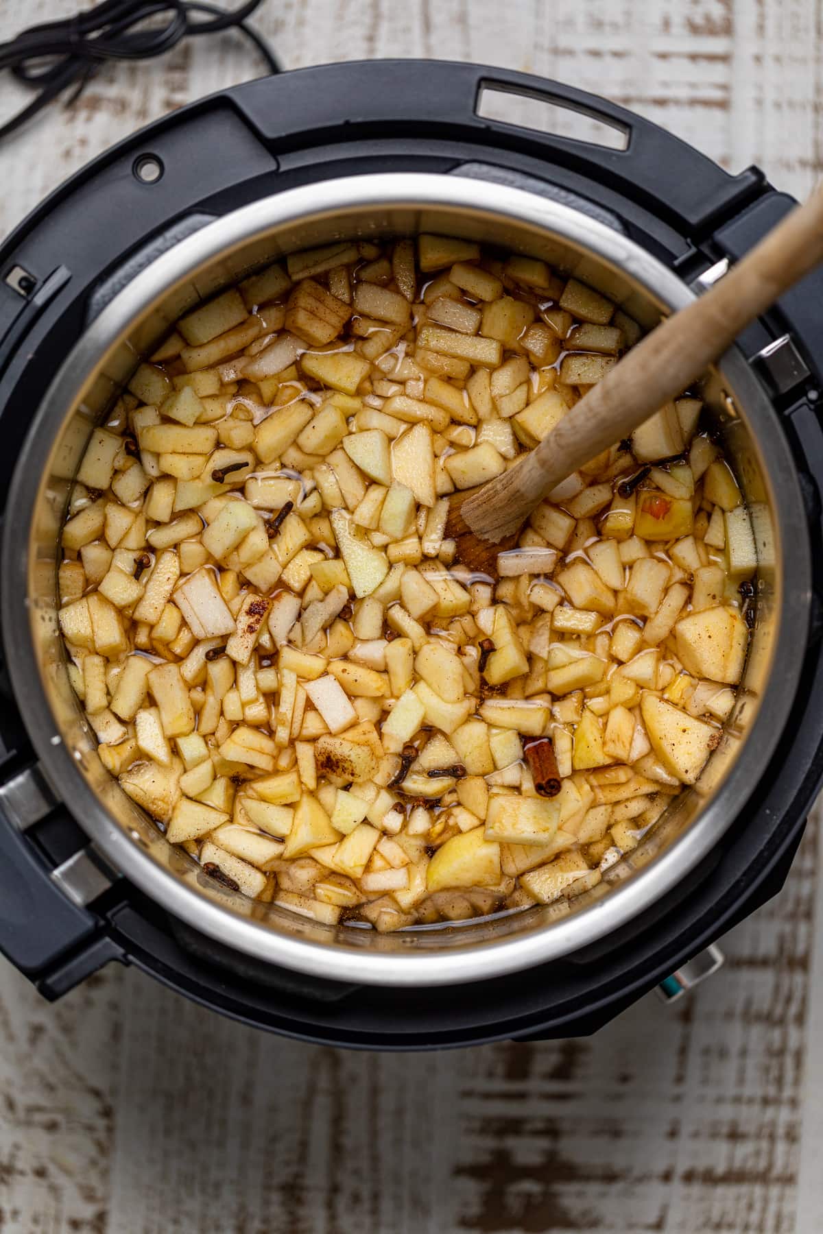 Wooden spoon stirring a slow cooker of apple pieces and spices.