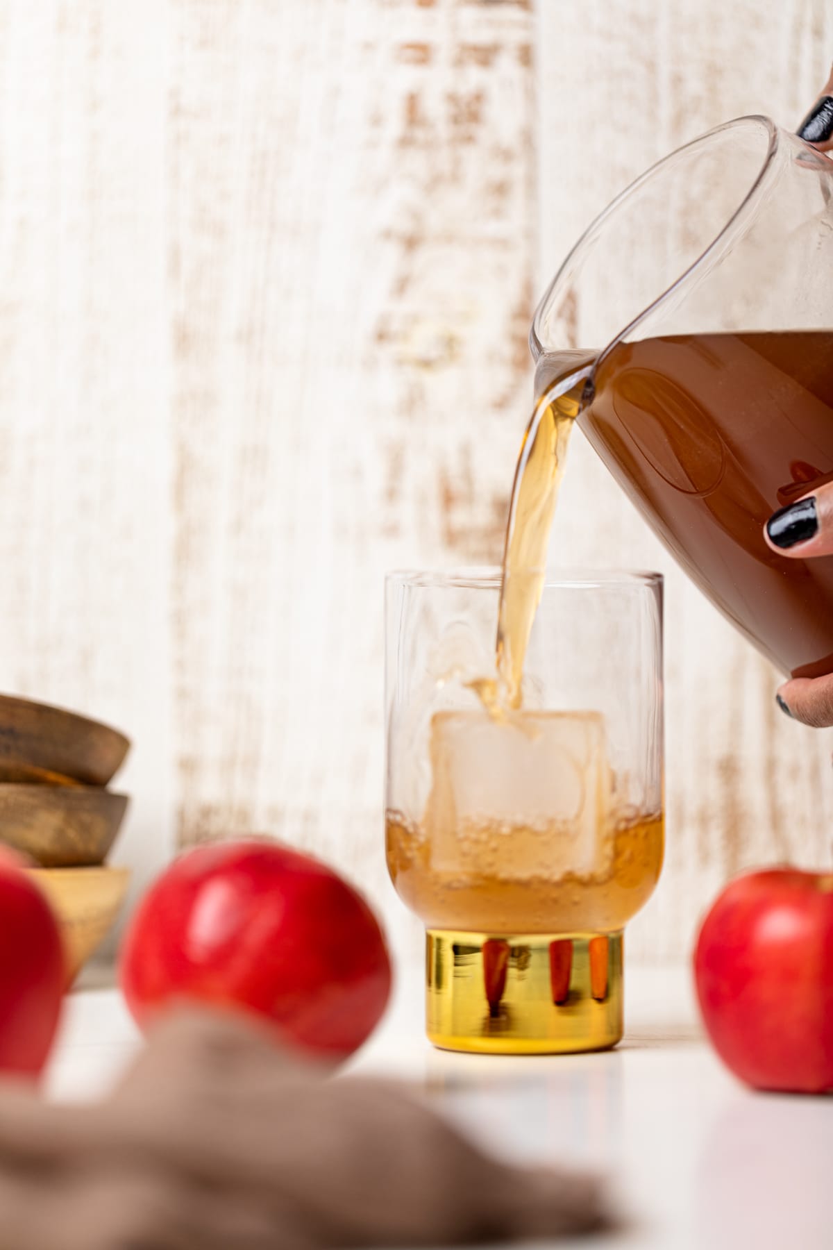 Glass pitcher pouring Homemade Slow Cooker Apple Cider into a glass with a gold base.