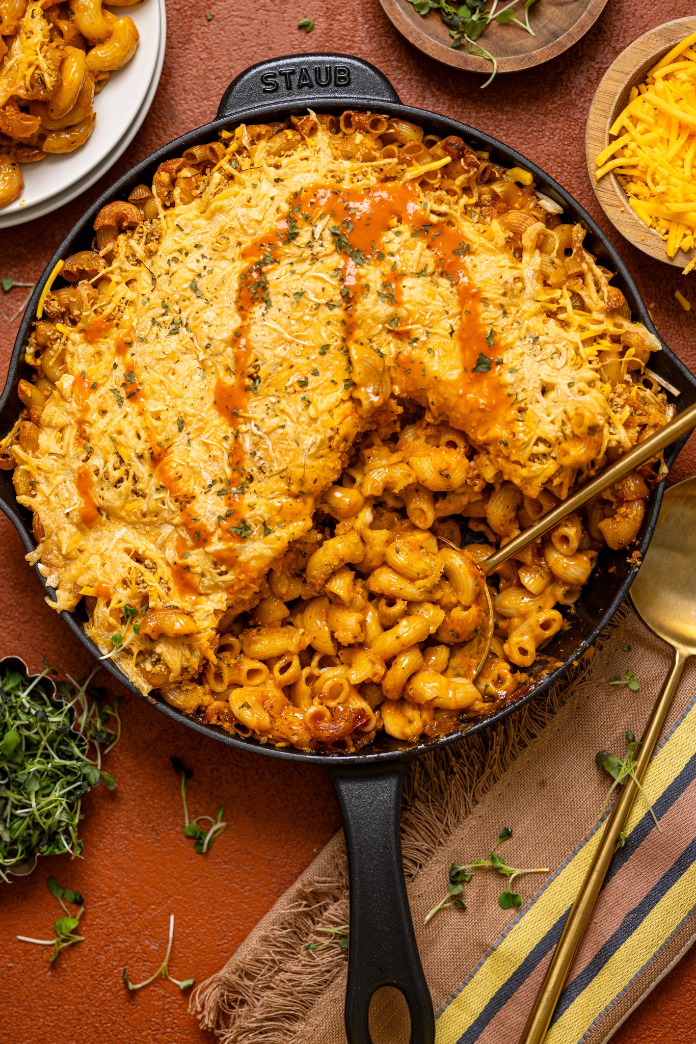 Baked Vegan Buffalo Mac + Cheese in a skillet scooped out with a spoon.