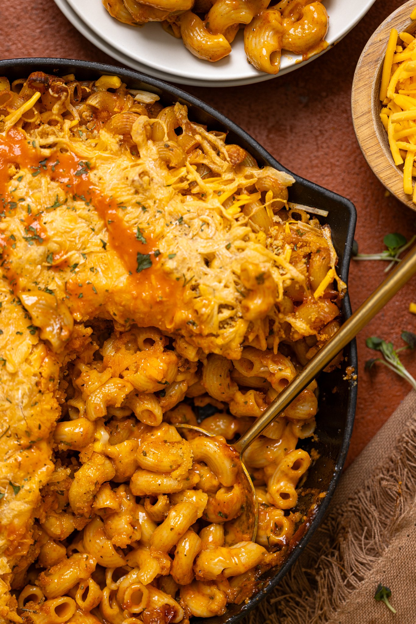 Baked Vegan Buffalo Mac + Cheese in a skillet scooped out with a spoon.