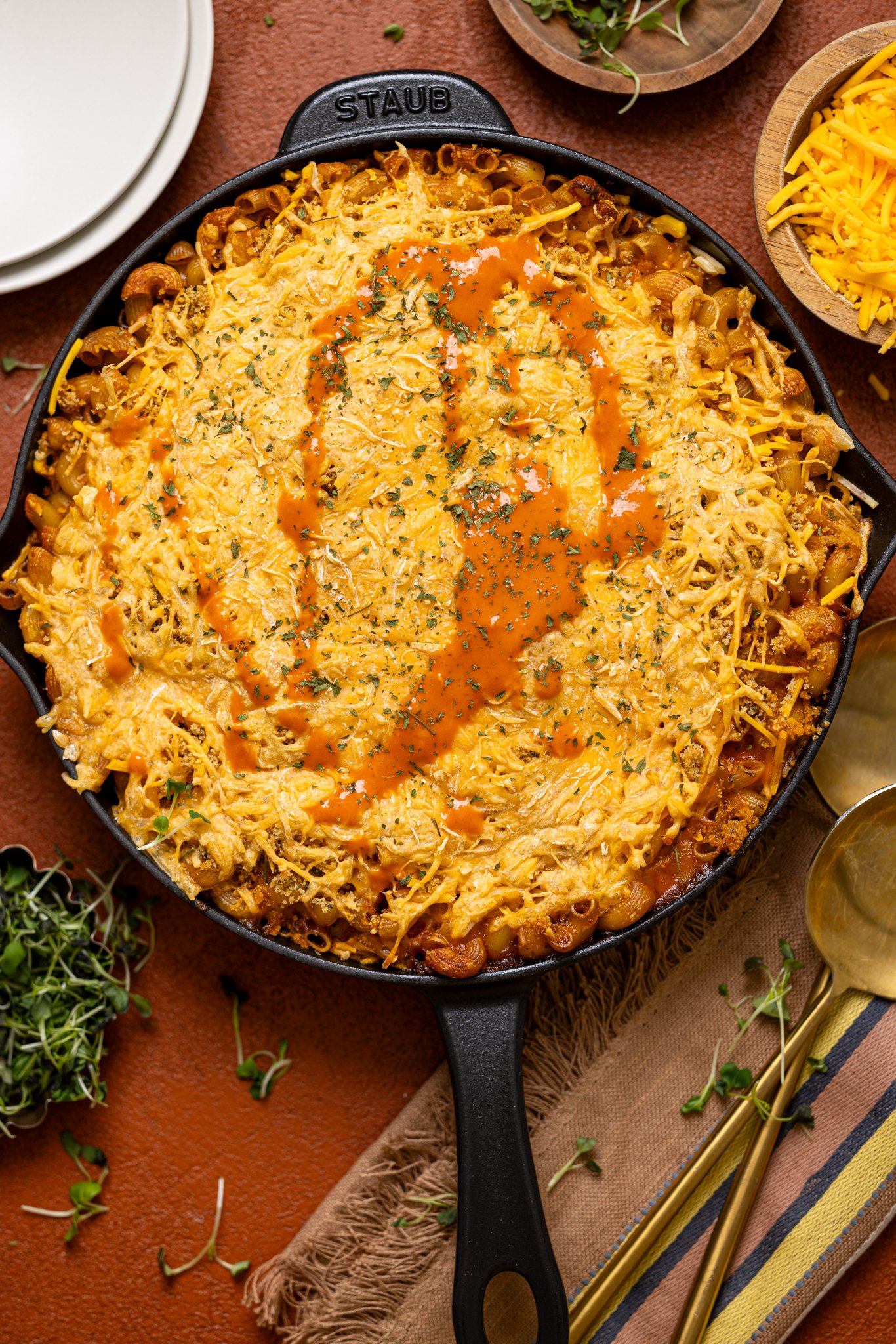 Baked Vegan Buffalo Mac + Cheese in a skillet with plates on the side.