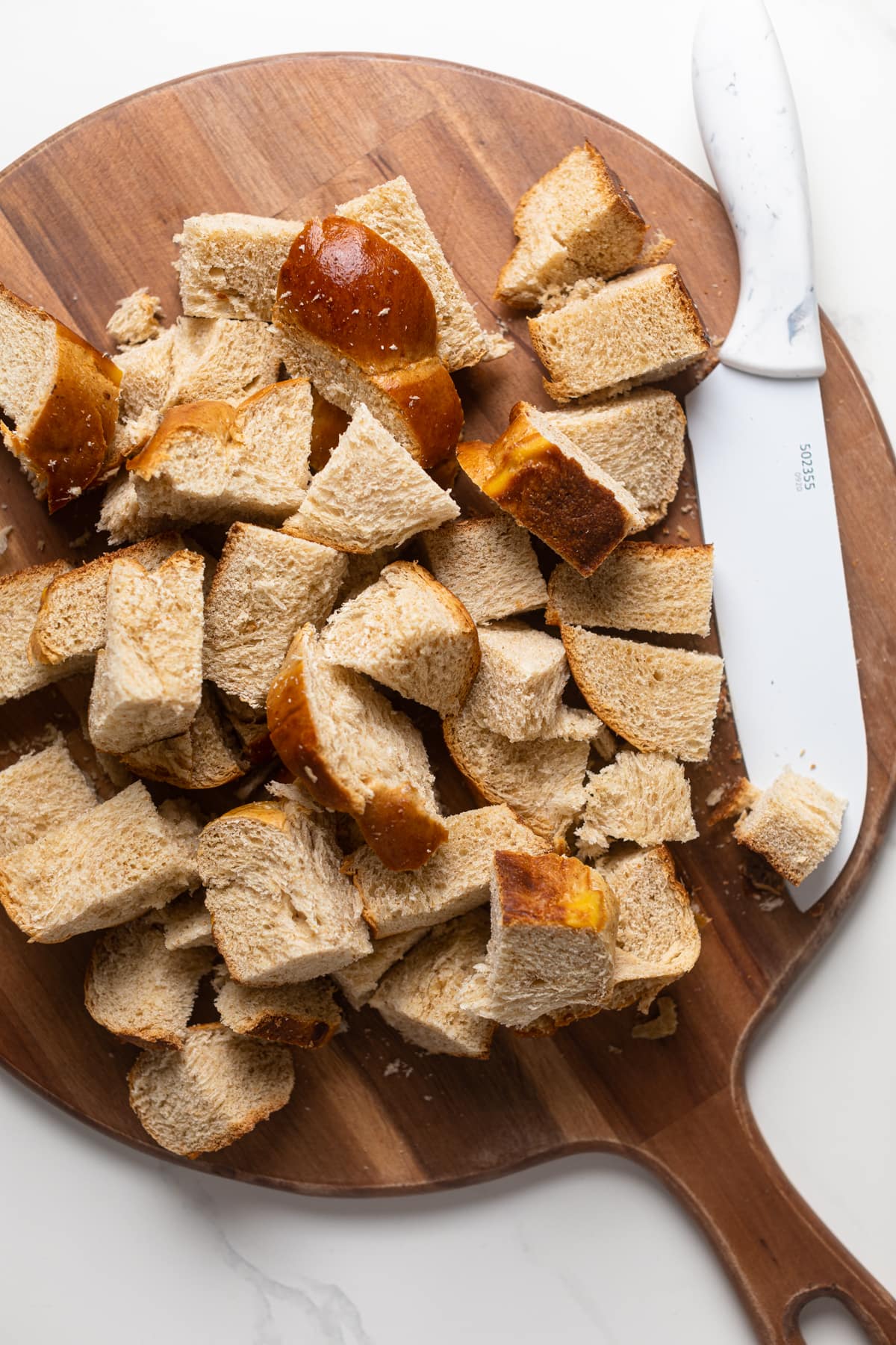 Pieces of challah bread and a knife on a wooden cutting board